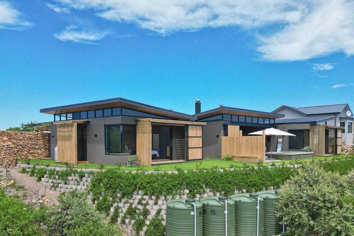 Modern architectural rear elevation featuring skillion roofs, timber slat privacy screens, large sliding glass doors, and integrated water storage tanks on a terraced site.