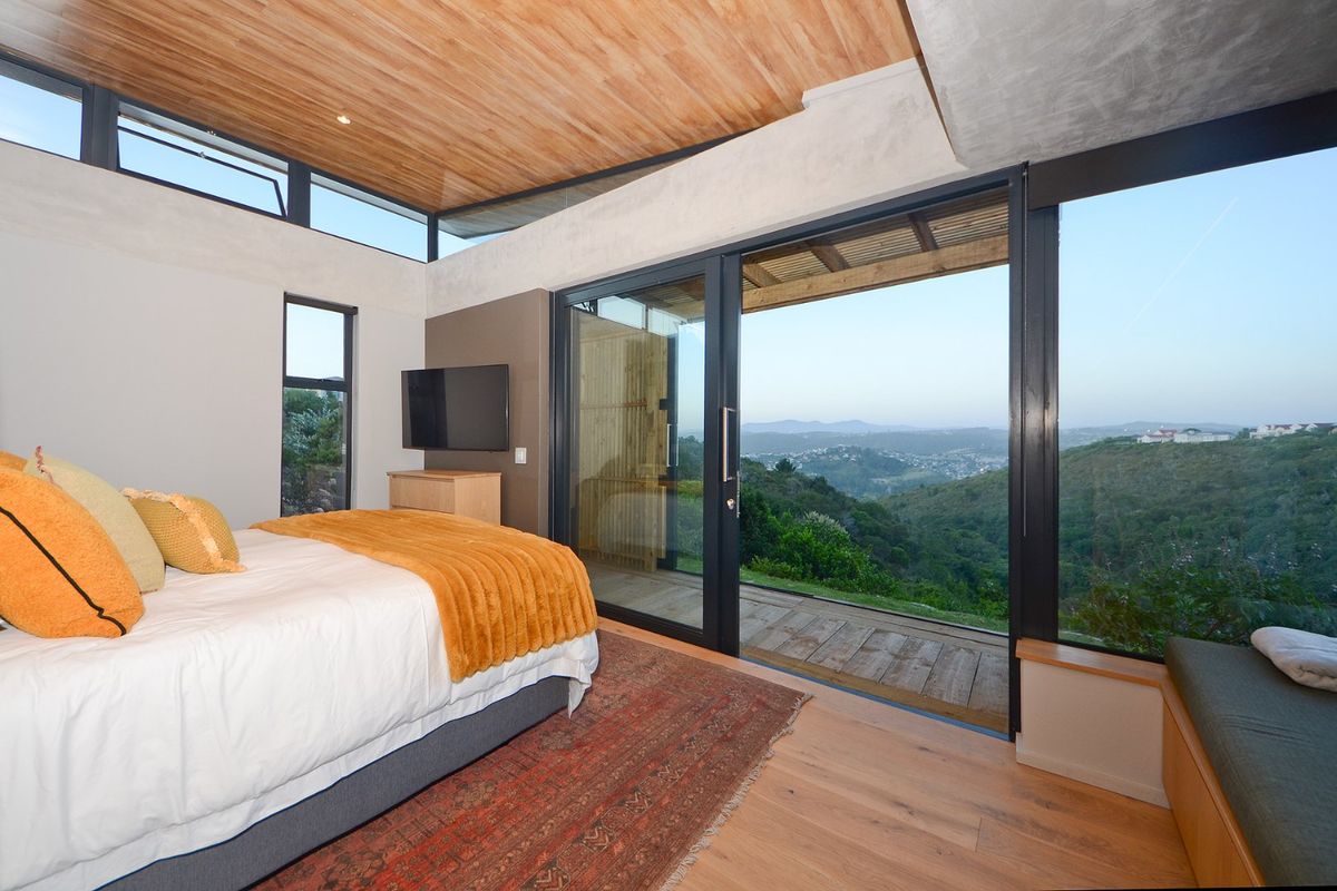 Modern bedroom featuring a timber ceiling, hardwood floors, and expansive sliding glass doors opening to a scenic mountain view.