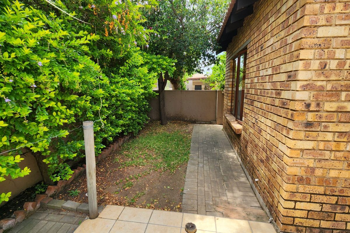A private rear garden area featuring a paved walkway, face brick exterior wall, and established perimeter hedging.