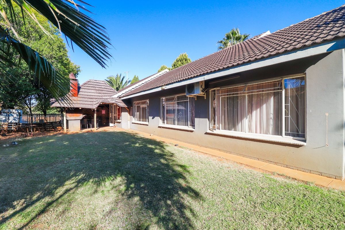 Rear view of the house featuring a tiled roof, large windows, and an attached outdoor entertainment area with a built-in braai.