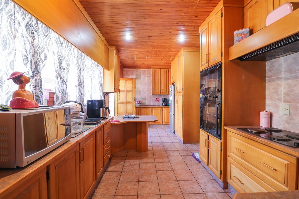 A traditional kitchen featuring extensive timber cabinetry, a wood-paneled ceiling, tiled flooring, and built-in oven and cooktop appliances.