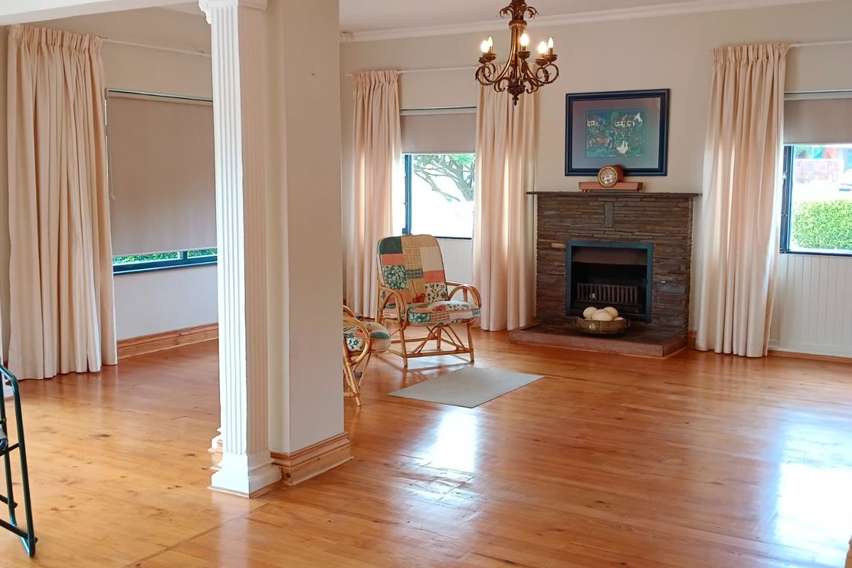 Spacious living area featuring polished timber flooring, a classic stone fireplace, and decorative columns, offering a bright and open layout.