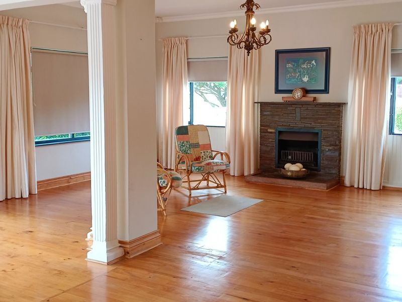 Spacious living area featuring polished timber flooring, a classic stone fireplace, and decorative columns, offering a bright and open layout.
