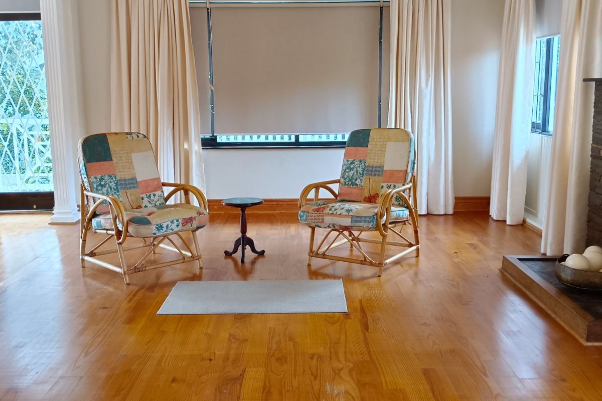 Spacious living room featuring polished timber flooring, a stone-clad fireplace, and large windows with neutral curtains, offering a bright and inviting atmosphere.