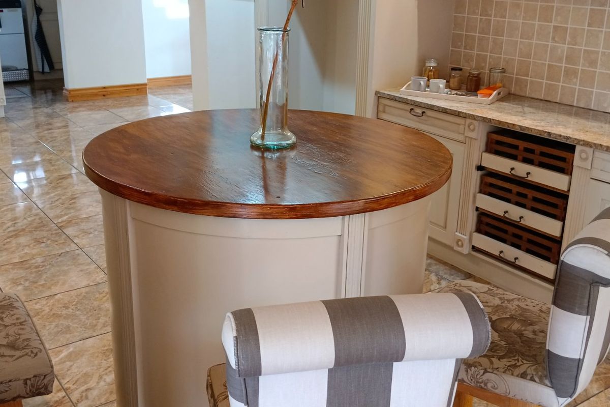 A kitchen featuring a central circular island with a wooden countertop, granite surfaces, tiled backsplash, and light-colored cabinetry.
