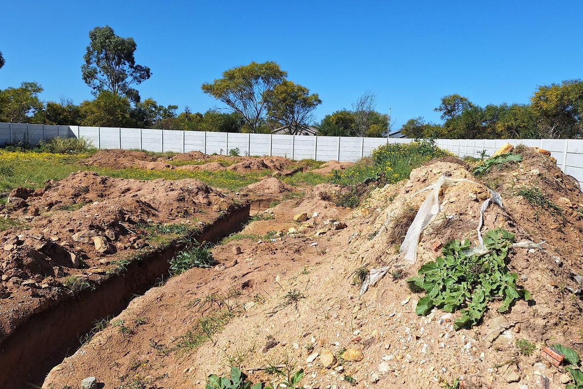Vacant residential land featuring a precast concrete boundary wall and excavated foundation trenches, ready for development.