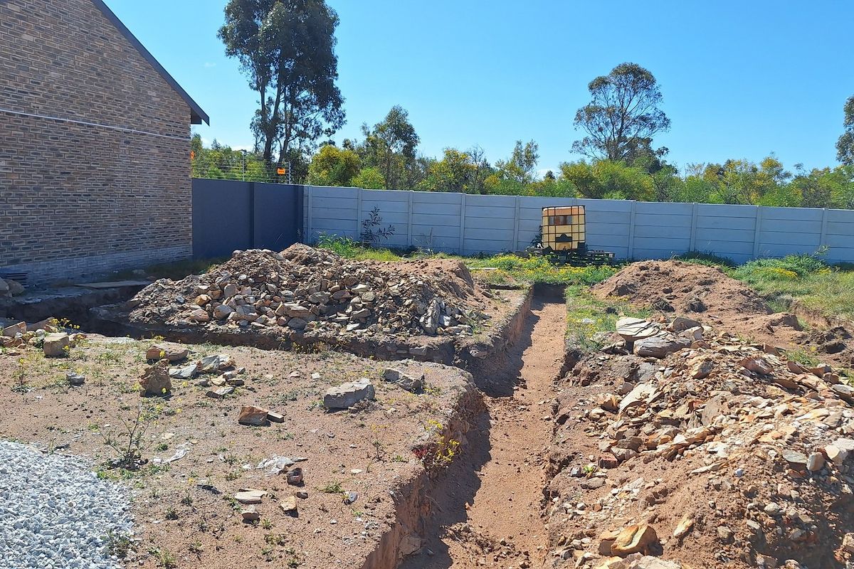 A vacant residential plot showing active foundation excavation work, enclosed by a precast concrete boundary wall.