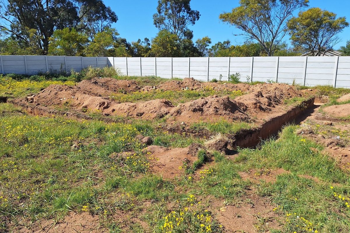 Vacant residential land featuring a precast concrete boundary wall and partially excavated foundation trenches ready for construction.