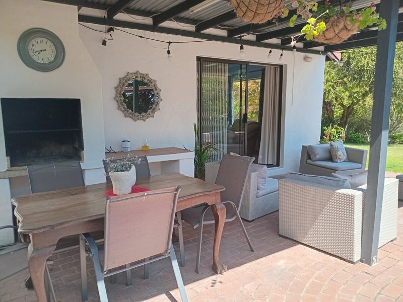Covered outdoor patio area featuring a built-in braai, brick paved flooring, and direct access to the interior through sliding glass doors.