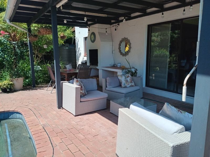 Covered outdoor patio area featuring a built-in braai, brick paving, and direct access to the swimming pool and interior living space.