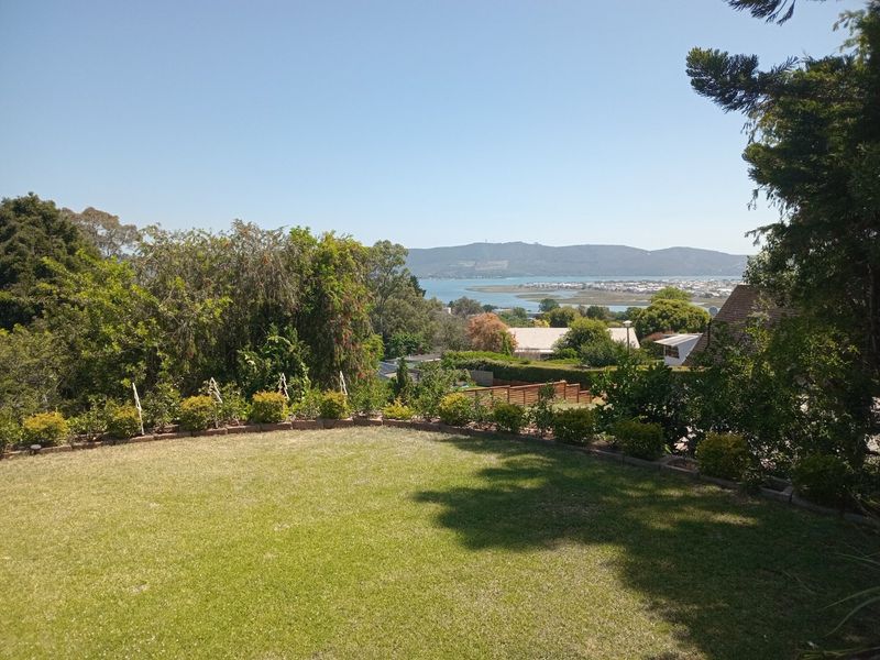 A scenic elevated view overlooking a lush green garden with a distant lagoon and mountain landscape in the background.