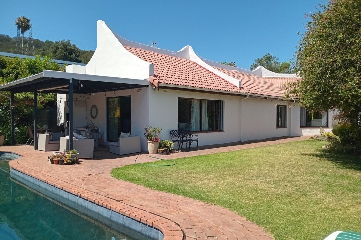 Rear view of the house featuring a swimming pool, covered patio area, and well-maintained garden with brick paving and traditional roof architecture.