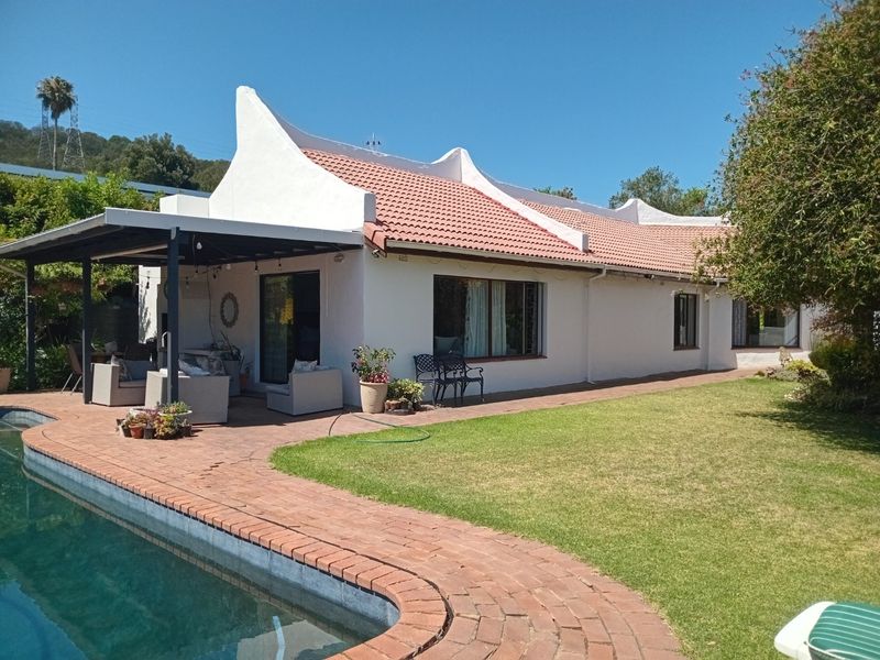 Rear view of the house featuring a swimming pool, covered patio area, and well-maintained garden with brick paving and traditional roof architecture.