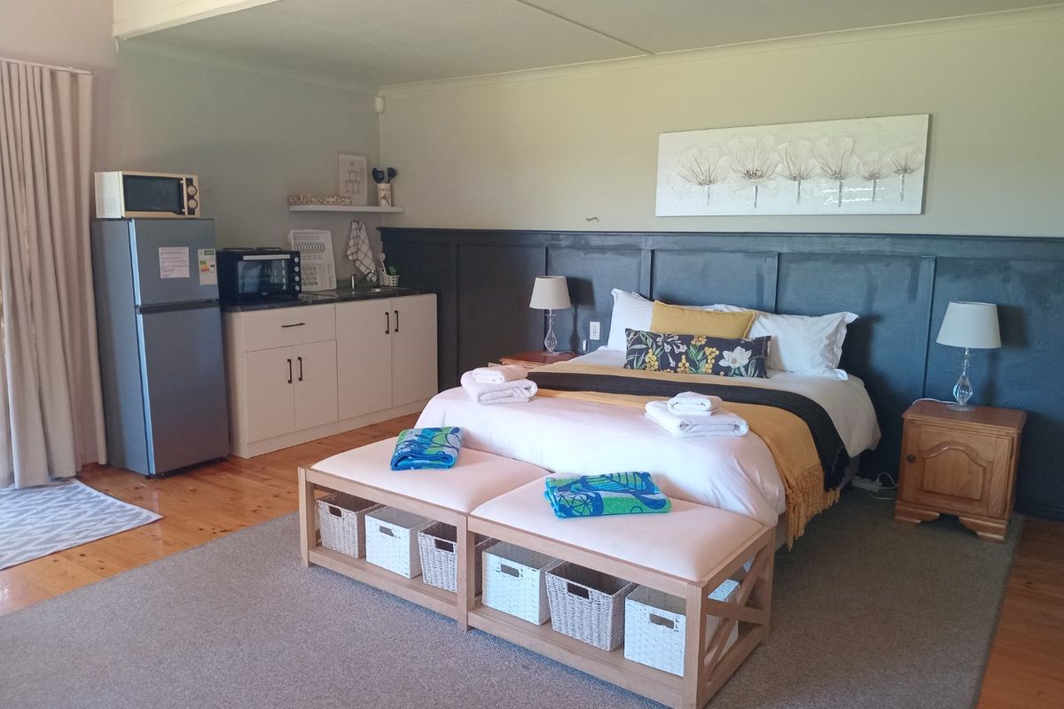A spacious bedroom featuring timber flooring, wainscoting, and a convenient built-in kitchenette area with sink and cabinetry.