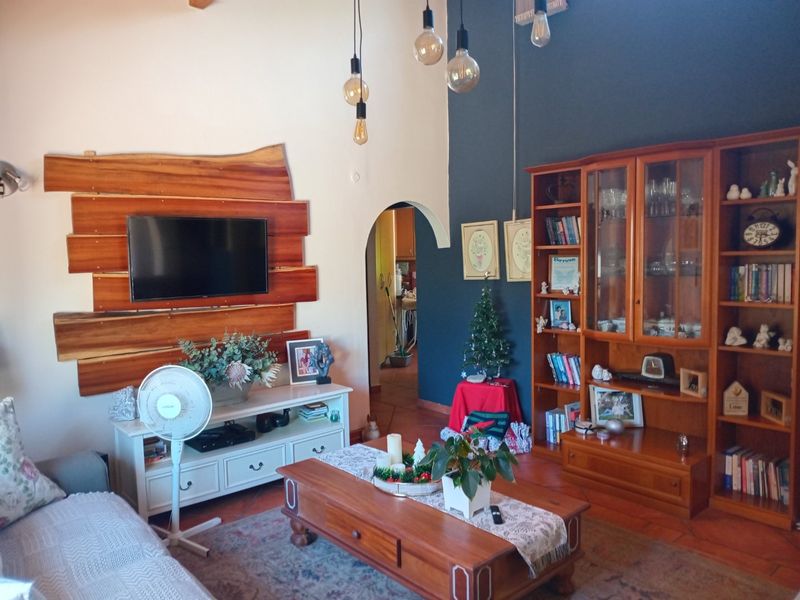 A cozy living room featuring an exposed timber feature wall, terracotta flooring, and a distinctive arched doorway leading to adjacent living spaces.