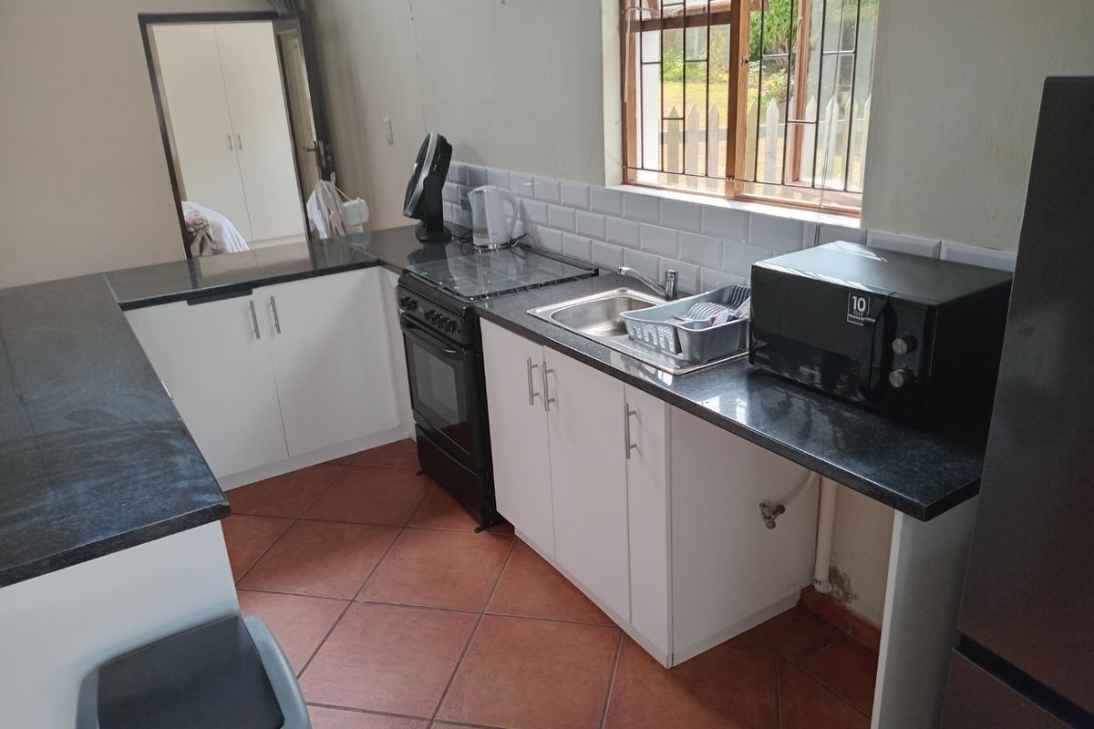 A functional kitchen featuring white cabinetry, dark granite countertops, subway tile backsplash, and tiled flooring, with a window providing natural light.