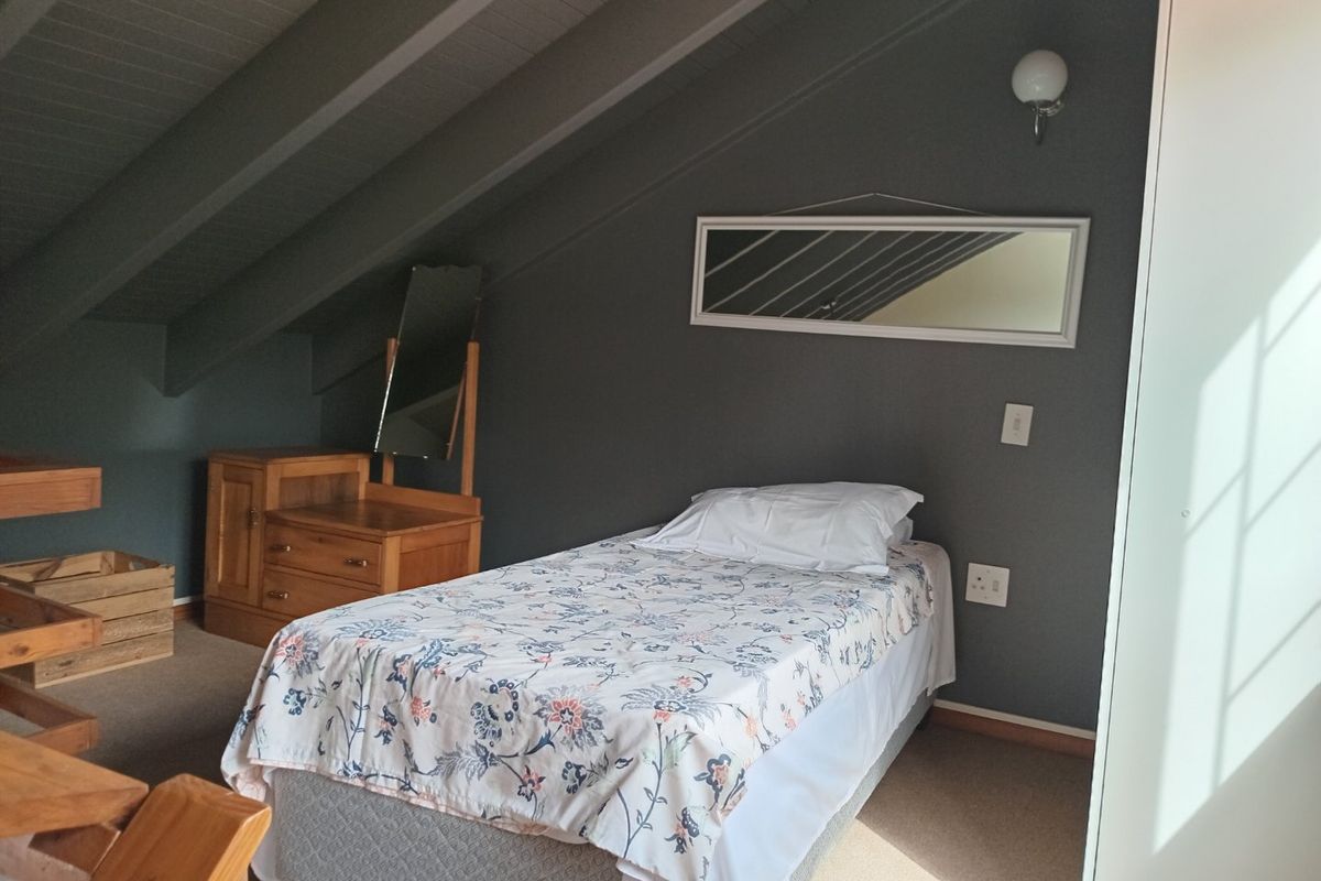 A cozy bedroom featuring a sloped ceiling with exposed rafters, dark grey walls, and a built-in wardrobe.
