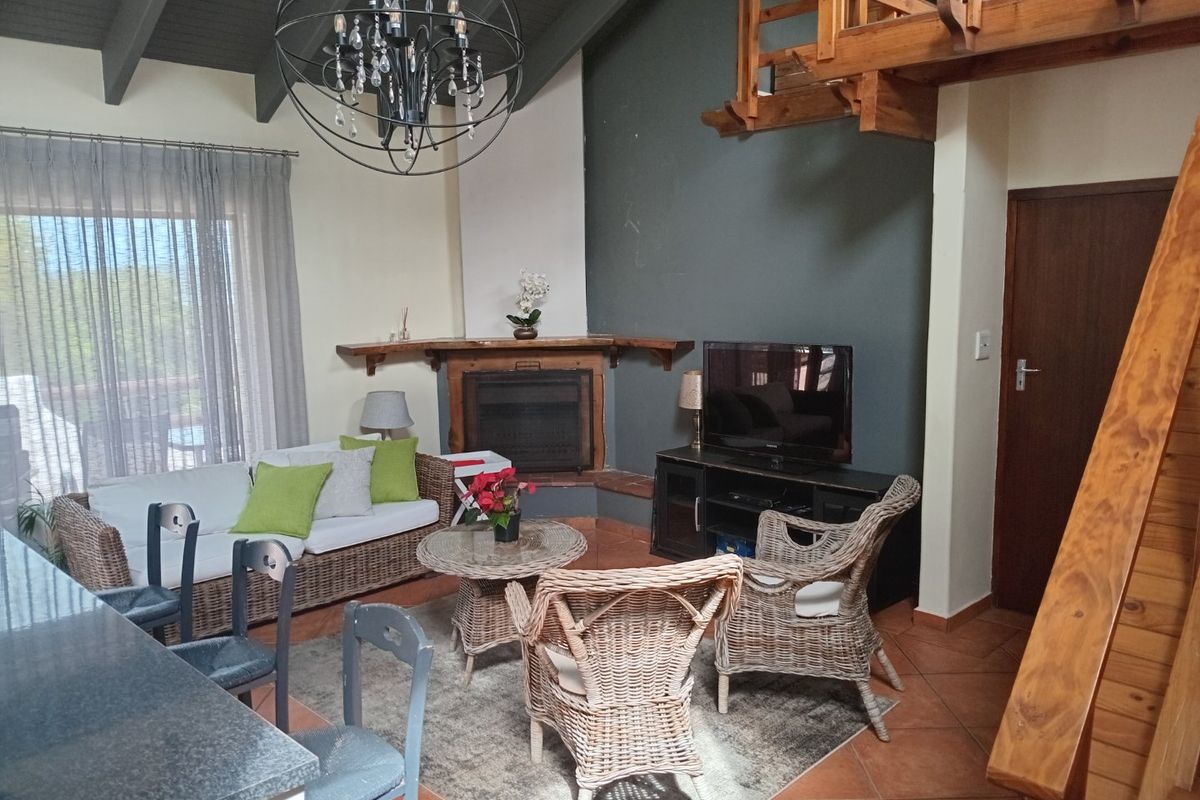 A cozy living room featuring a corner fireplace, exposed timber ceiling beams, and a wooden staircase leading to an upper level.