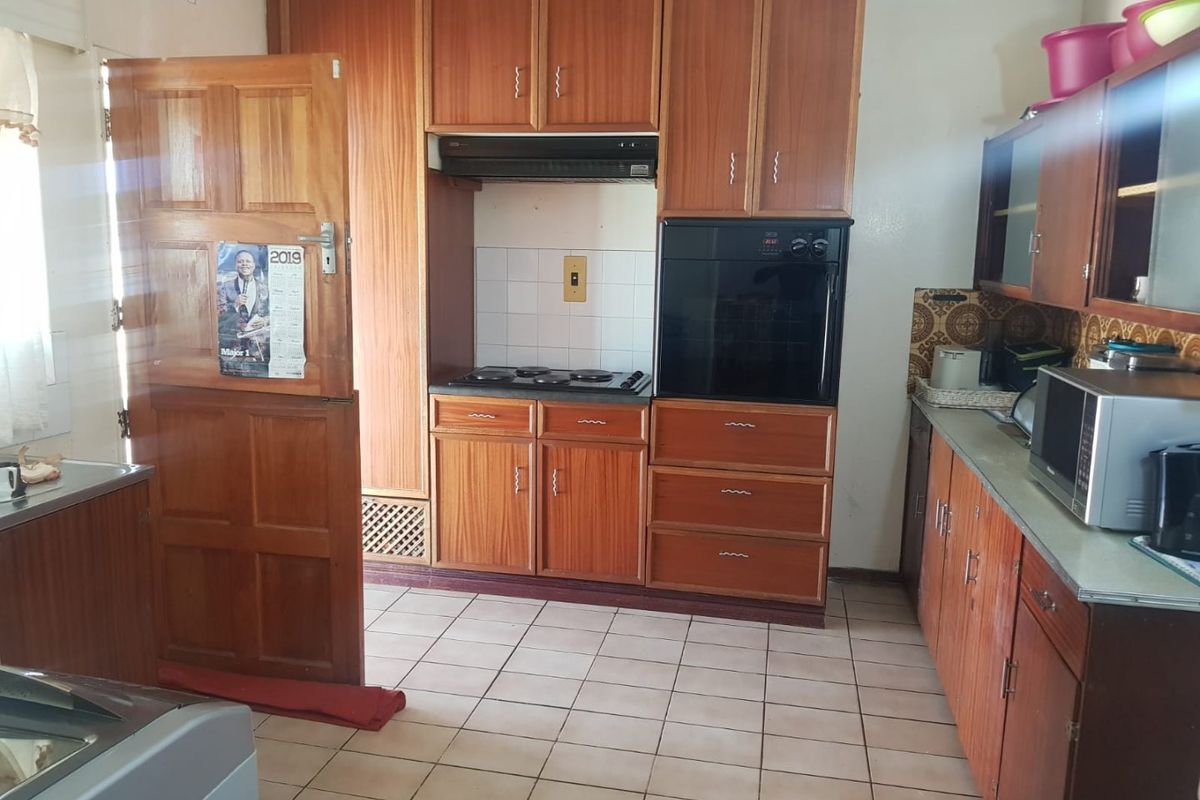 A functional kitchen featuring wooden cabinetry, built-in oven, electric hob, and tiled flooring, offering a dated aesthetic ready for modernization.