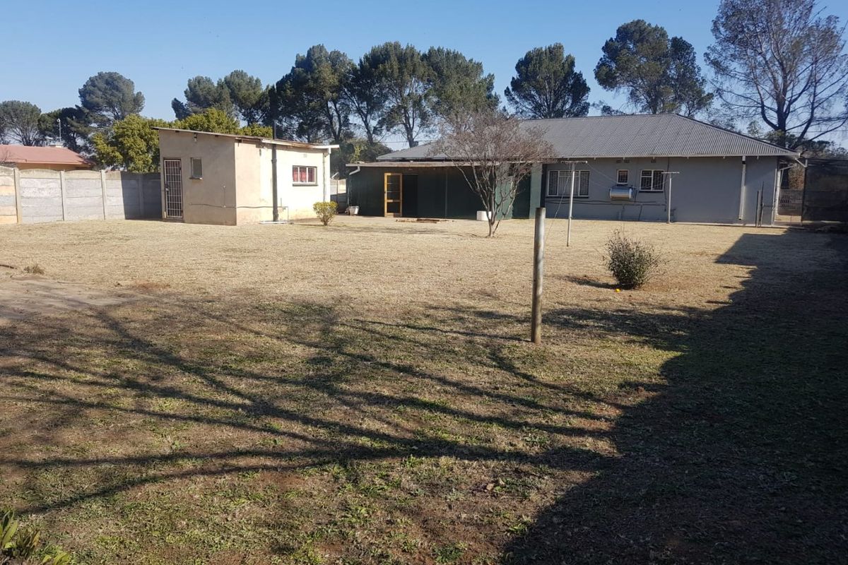 Spacious rear garden featuring a large lawn, a detached outbuilding, and a covered patio area attached to the main house.
