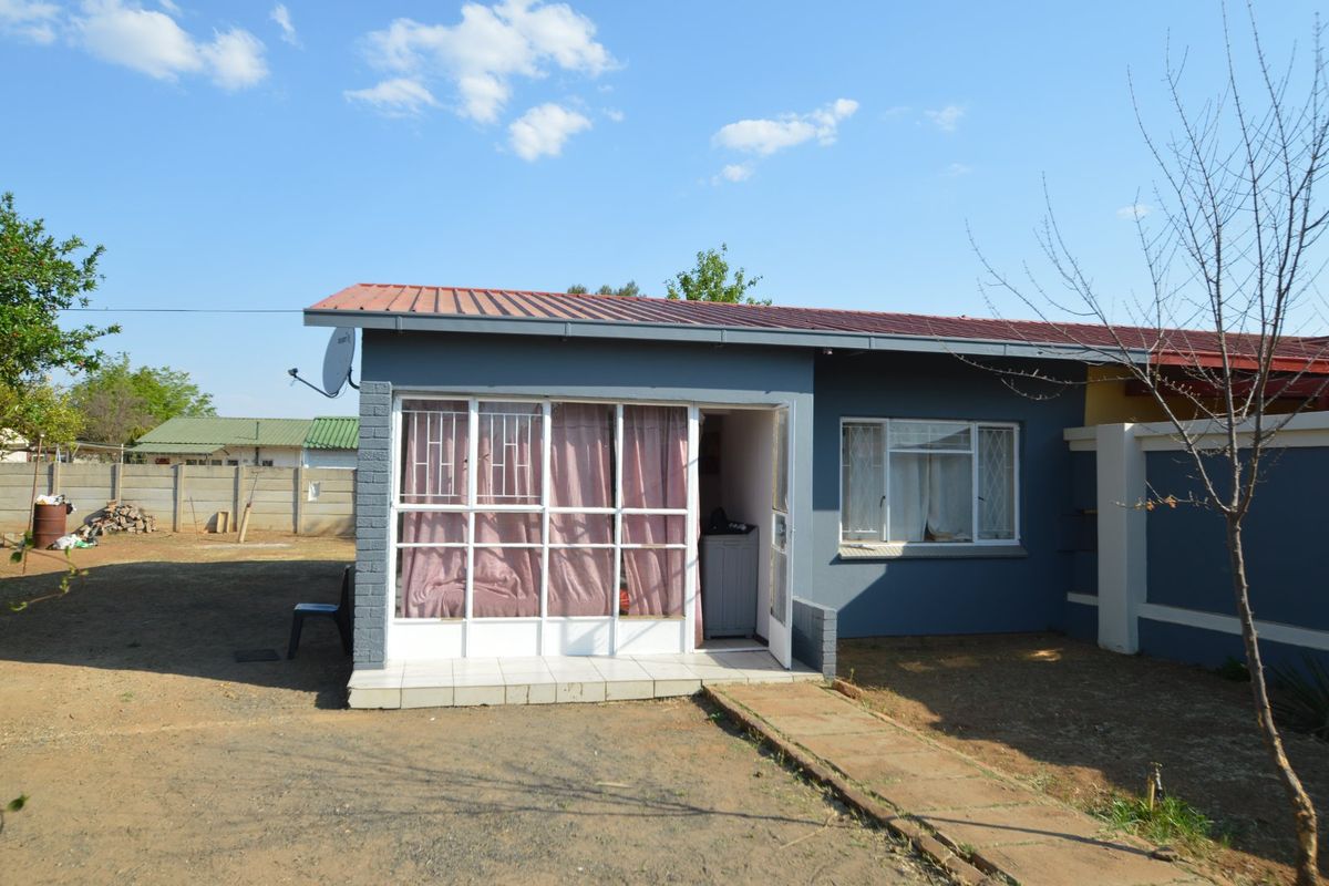 Rear view of the apartment featuring a small tiled patio, metal roofing, and security features on windows and doors.