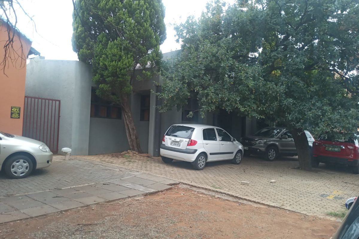 Front exterior view of the commercial property featuring a paved parking area, mature trees, and a secure gated entrance.