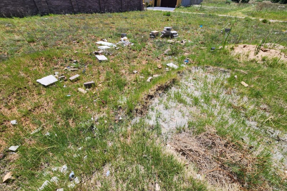 A vacant residential plot featuring natural grass cover and a perimeter boundary wall, requiring site clearing and preparation for development.