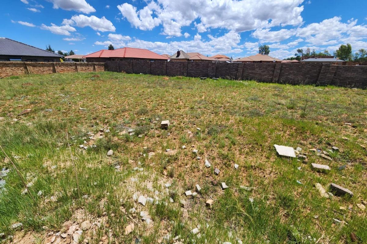 A vacant residential plot featuring natural grass cover and a secure perimeter brick wall, ready for development.