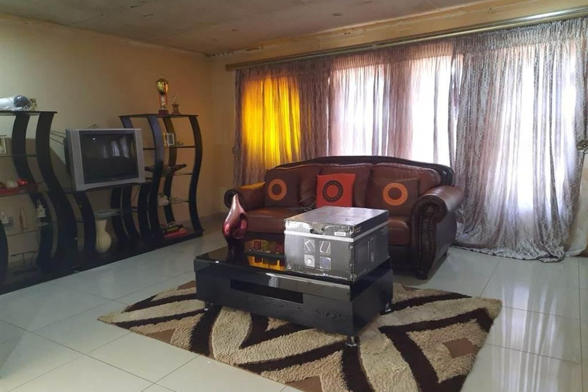 A living room featuring tiled flooring and large windows, currently showing signs of wear on the ceiling finish.