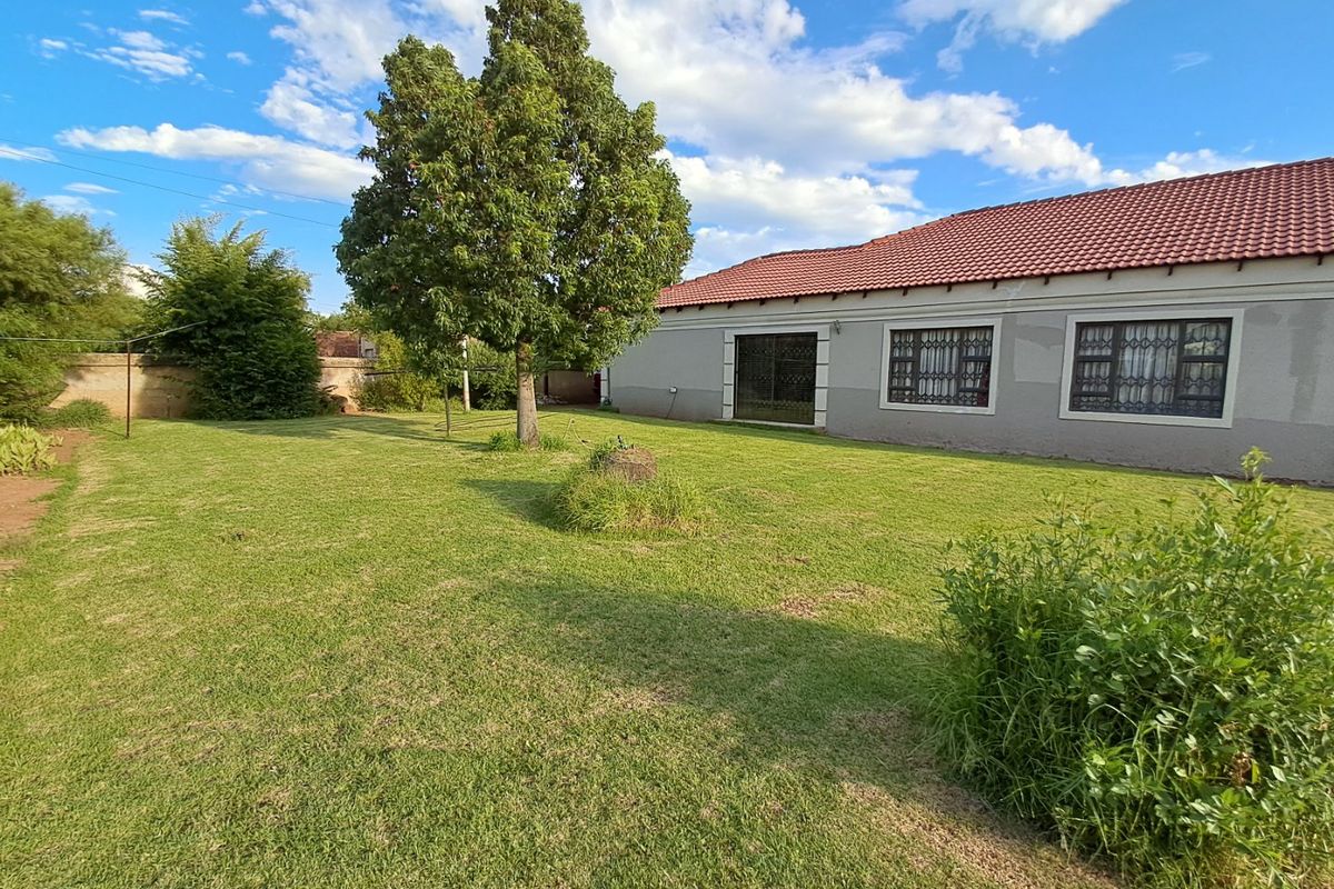 A spacious rear garden featuring a well-maintained lawn, mature tree, and the rear elevation of the house with tiled roofing and security-fitted windows.