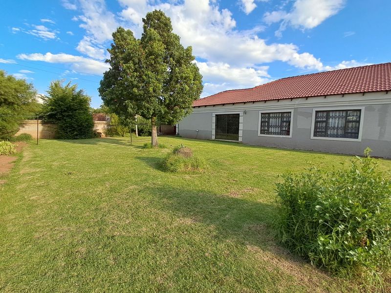 A spacious rear garden featuring a well-maintained lawn, mature tree, and the rear elevation of the house with tiled roofing and security-fitted windows.