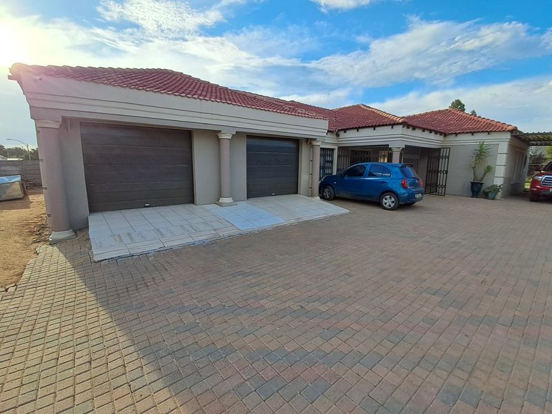 Front view of a residential property featuring a double garage, tiled roof, and a spacious paved driveway.