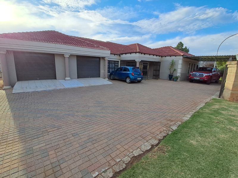 Front exterior view of a residential house featuring a double garage, paved driveway, and a covered carport area.