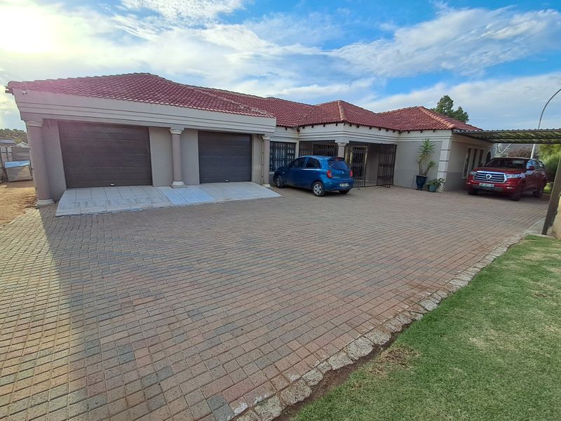 Front elevation of a residential property featuring a double garage, extensive paved driveway, and a covered carport area.