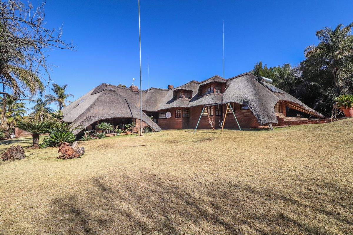 Rear view of a traditional brick house featuring a distinctive thatched roof, dormer windows, and a spacious surrounding garden area.