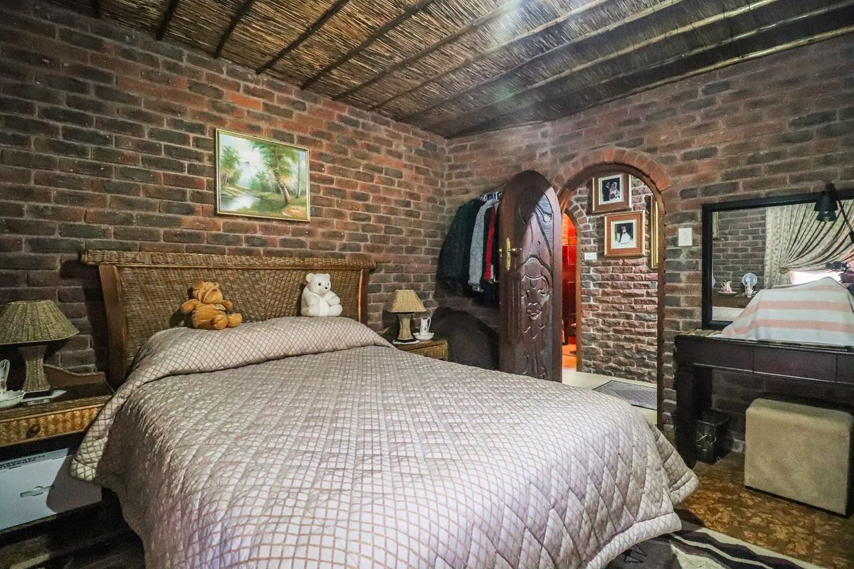 A rustic bedroom featuring exposed brick walls, a traditional thatched ceiling, and a distinctive arched doorway with a carved wooden door.