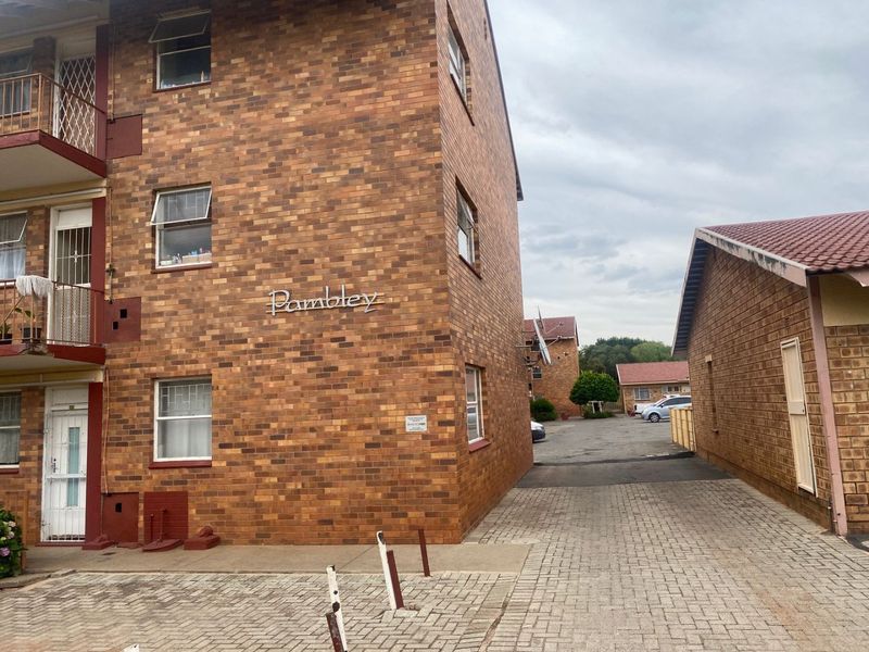 Exterior view of the Pambley apartment complex featuring face brick construction, paved driveway access, and balcony access for upper-level units.