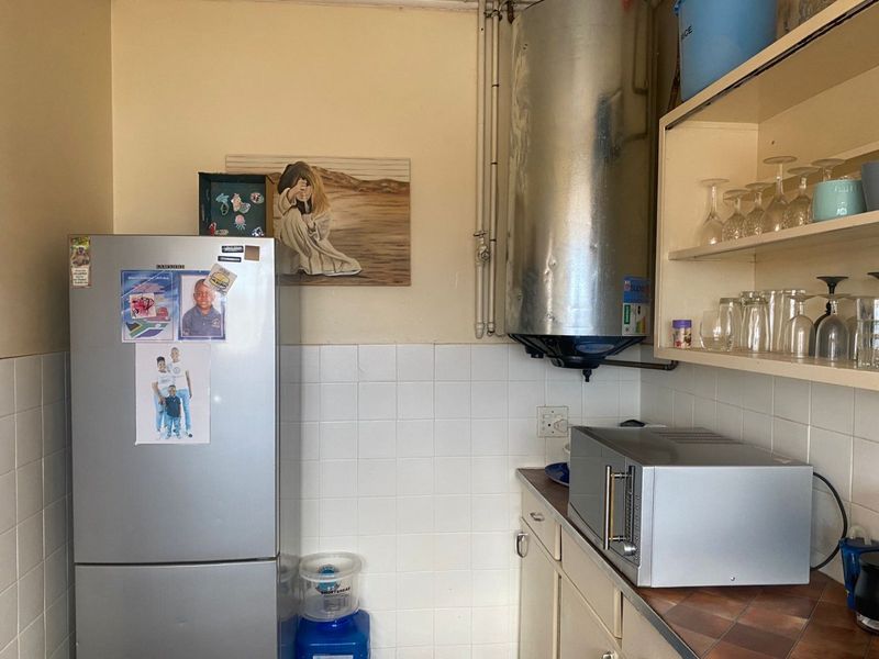 A functional kitchen area featuring a wall-mounted electric water heater, tiled splashback, and built-in shelving units.