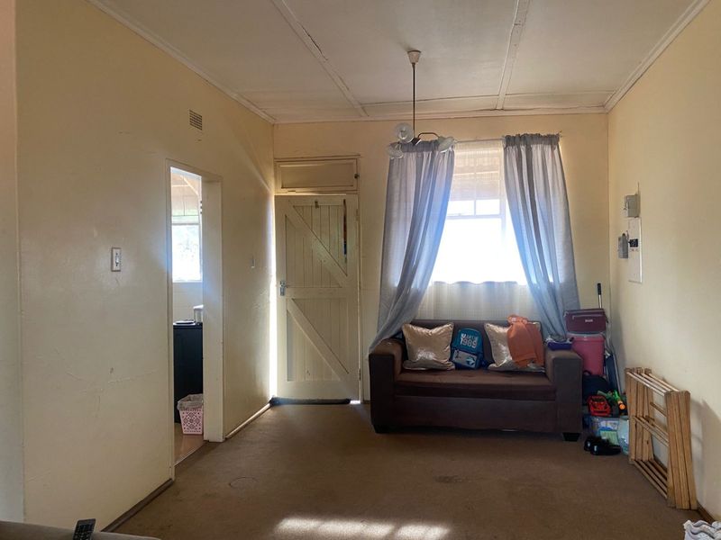 A living room featuring dated carpet flooring, original timber door, and visible wall cracks, offering potential for renovation and modernization.