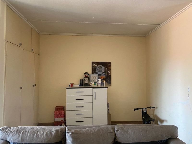 A bedroom featuring built-in cupboards and ceiling cornice, currently showing signs of wear including peeling wall paint and ceiling damage.