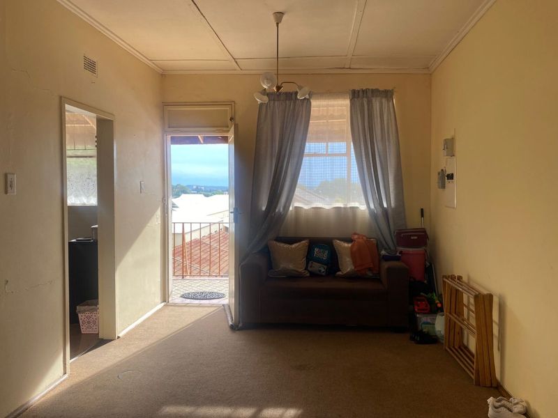 A living room featuring carpet flooring, direct balcony access, and dated finishes, offering potential for modernization and cosmetic updates.