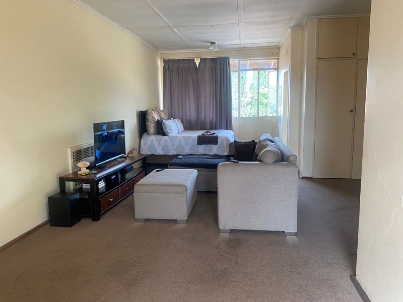 Open-plan studio apartment featuring built-in storage cupboards and a wall-mounted air conditioning unit, requiring cosmetic updates to the flooring and ceiling finishes.