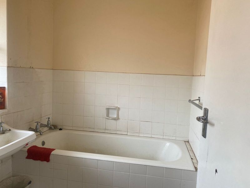 A dated bathroom featuring a built-in bathtub and wall-mounted basin, requiring cosmetic updates and repairs to the tiling and wall finishes.