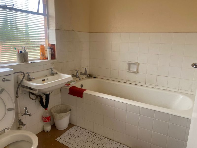 A dated bathroom featuring a built-in bathtub, wall-mounted basin, and tiled walls, requiring renovation to update the finishes and plumbing fixtures.