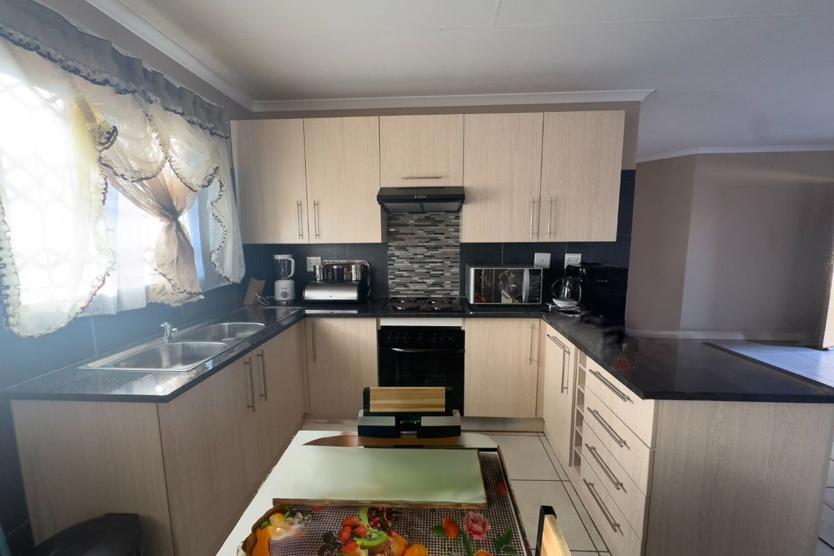A functional kitchen featuring light wood-finish cabinetry, granite countertops, a double sink, and built-in cooking appliances with a tiled backsplash.