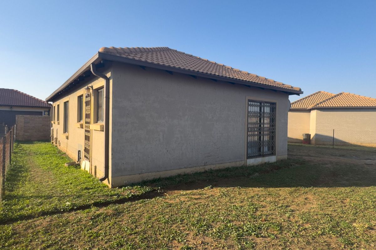 Rear view of the house featuring plastered walls, a tiled roof, and a security gate leading to the backyard area.