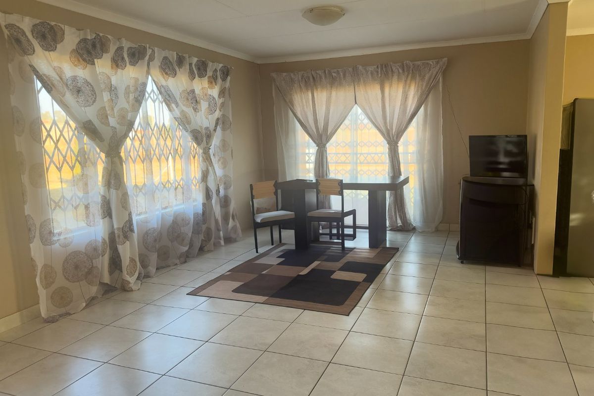 A spacious living area featuring neutral tiled flooring, large windows with security gates, and ample natural light.