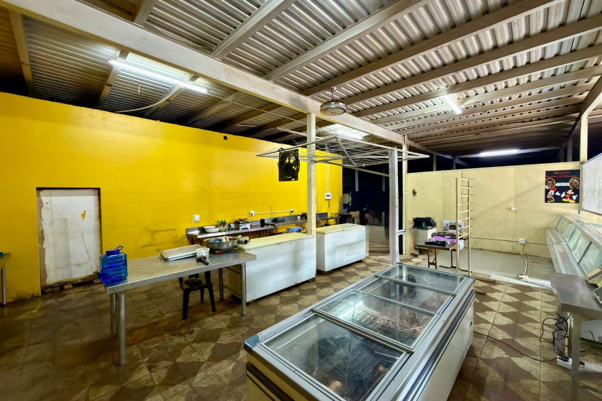 Commercial kitchen space featuring exposed metal roofing, tiled flooring, and stainless steel prep areas, suitable for food service operations.