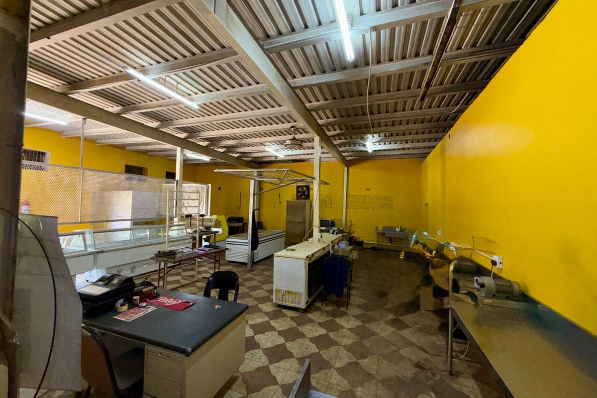 Commercial utility or prep space featuring exposed steel roof trusses, tiled flooring, and functional stainless steel surfaces, suitable for various industrial or retail applications.