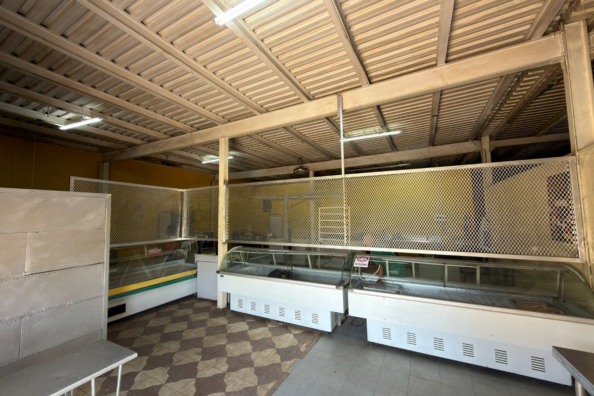 Commercial utility space featuring multiple refrigerated display counters, metal security partitions, and an exposed industrial steel roof structure.